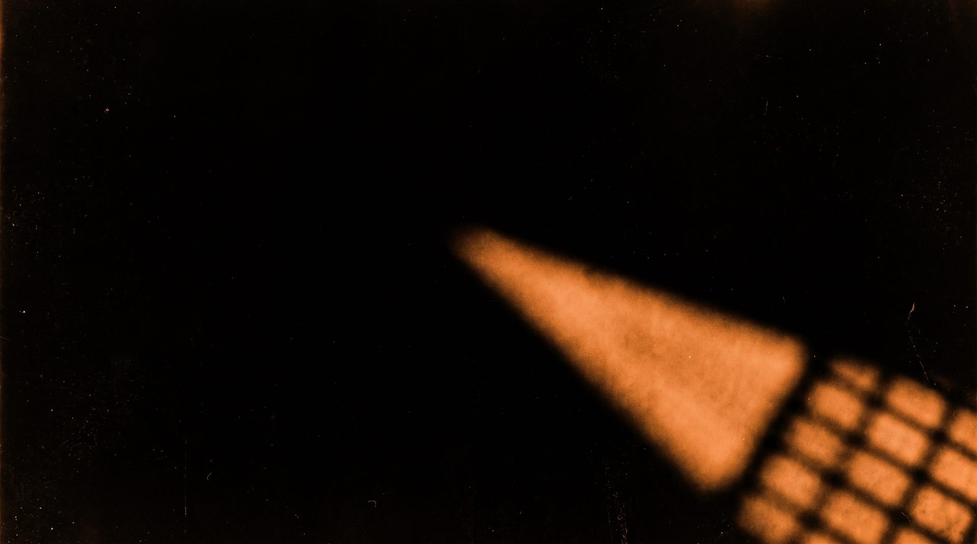 Photogram: a single hard beam of sodium light crosses the dark and breaks over a steel walkway grating.